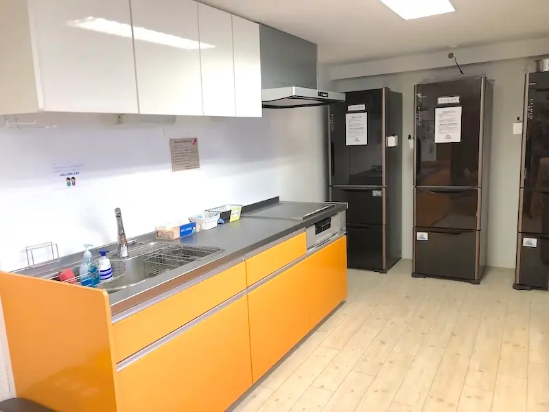 オレンジ色のキッチン、ブラウンの冷蔵庫3台が置いてある共有キッチンの写真