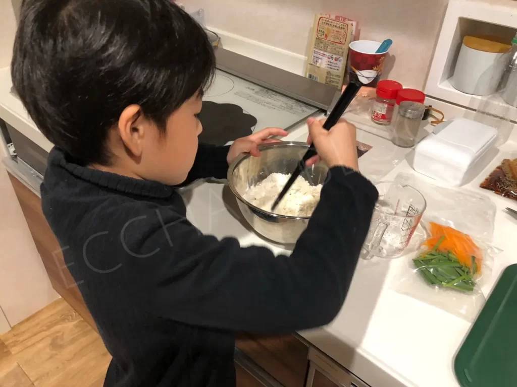 小学生低学年の男の子がチヂミ粉を箸で混ぜている写真。