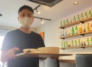 韓国料理コッキルのオーナーシェフ、ジェホさんがマスクをつけて食事を運んでいる写真