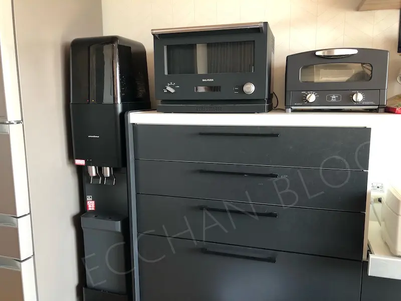左から順に、冷蔵庫、アマダナウォーターサーバー（黒）、バルミューダの電子レンジ、アラジンのトースターが置いてあるキッチンの写真